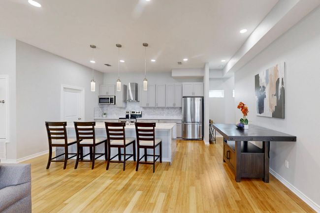 Kitchen featuring appliances with stainless steel finishes, wall chimney exhaust hood, light wood-style flooring, a breakfast bar, and backsplash | Image 20