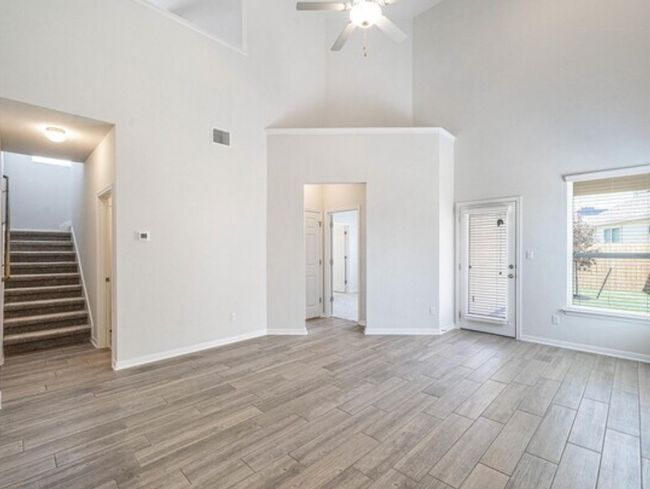 Unfurnished living room featuring high vaulted ceiling, ceiling fan, stairway, and light wood-type flooring | Image 6