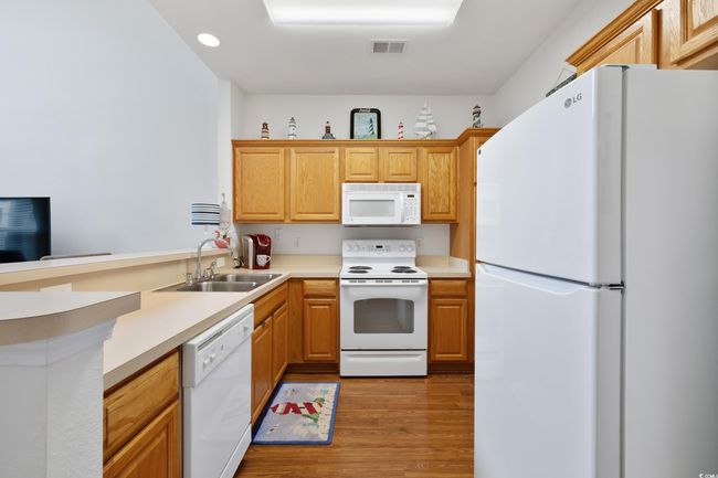 Kitchen with white appliances, a sink, light wood-style flooring, a peninsula, and light countertops | Image 13