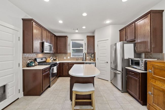 Kitchen with light countertops, a sink, a kitchen island, stainless steel appliances, and decorative backsplash | Image 10