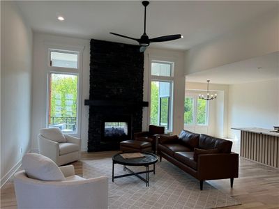 Living room featuring light hardwood / wood-style floors, ceiling fan with notable chandelier, a multi sided fireplace, and plenty of natural light | Image 1