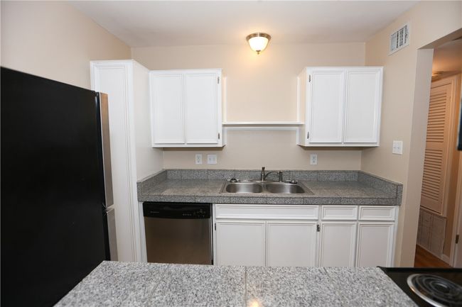 Galley kitchen has a refrigerator and full-sized range, with granite tile countertops and plenty of storage space. | Image 4