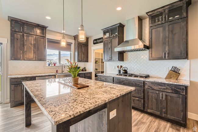 Kitchen featuring wall chimney exhaust hood, appliances with stainless steel finishes, light stone countertops, backsplash, and a kitchen island | Image 6