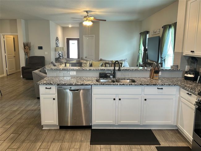 Kitchen with stainless steel dishwasher, open floor plan, a sink, ceiling fan, and dark stone counters | Image 4