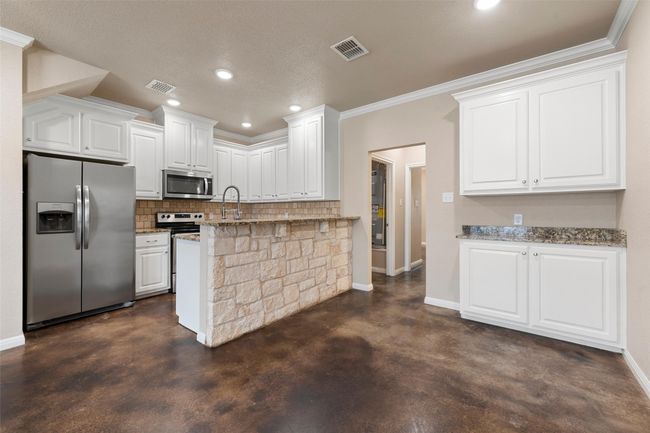 Kitchen featuring appliances with stainless steel finishes, finished concrete flooring, decorative backsplash, white cabinets, and light stone counters | Image 6