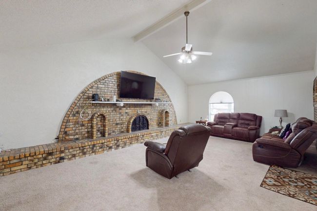 Living area featuring a fireplace, ceiling fan, vaulted ceiling with beams, and light carpet | Image 7