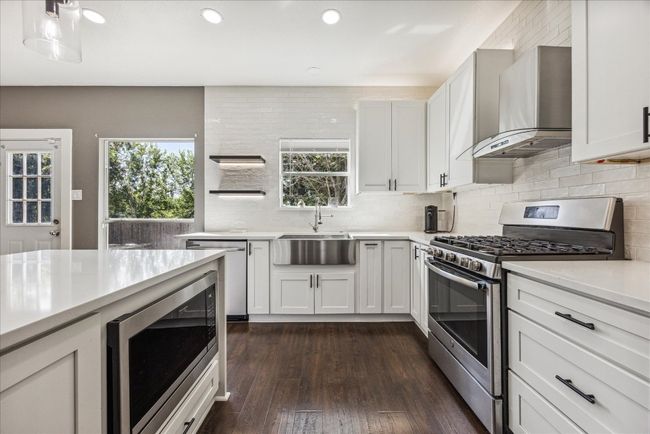 Kitchen featuring a sink, decorative backsplash, stainless steel appliances, light countertops, and wall chimney exhaust hood | Image 14