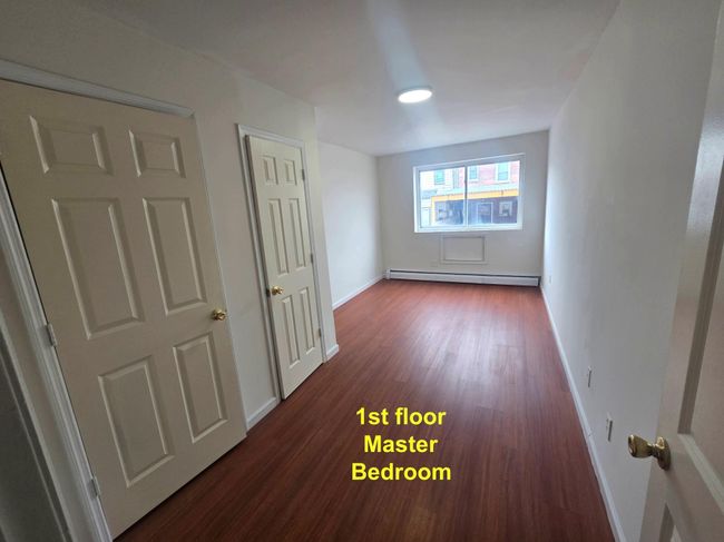 Unfurnished bedroom with baseboard heating, dark wood-type flooring, and baseboards | Image 9