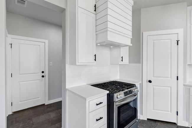 Kitchen with gas range, custom exhaust hood, light countertops, white cabinetry, and backsplash | Image 18