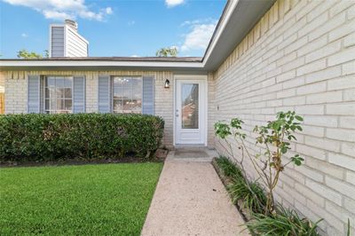 The inviting entrance is framed by mature bushes, coordinating shutters, and classic white brickwork. | Image 3