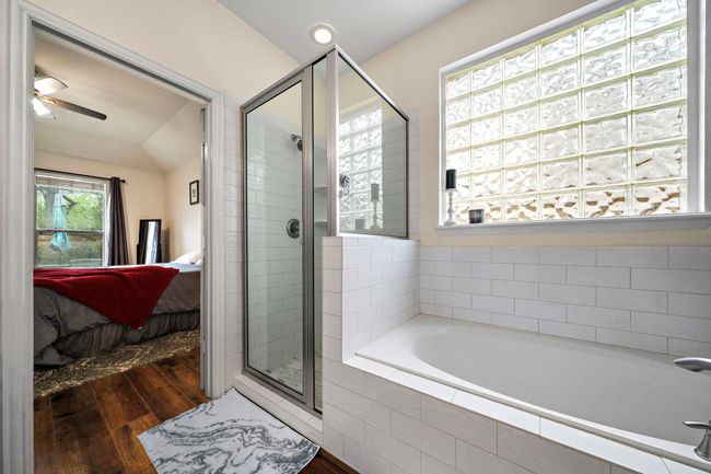 This spacious bathroom features a modern glass-enclosed shower, a luxurious soaking tub, and a long granite vanity with ample storage. The large window provides natural light. | Image 13