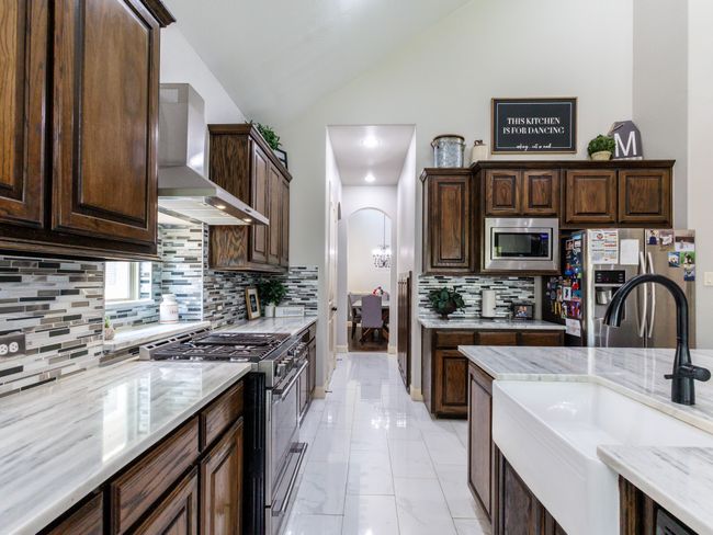 The kitchen is well-lit and features stunning granite countertops, a farmhouse sink, and tile flooring throughout. | Image 11