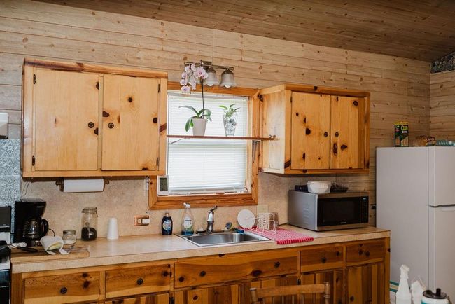 Kitchen featuring stainless steel microwave, freestanding refrigerator, light countertops, wooden walls, and decorative backsplash | Image 8