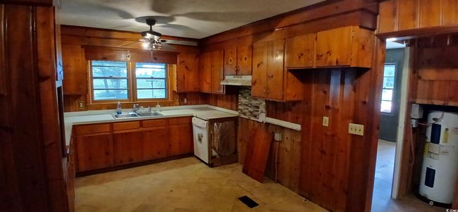 Kitchen with under cabinet range hood, brown cabinets, ceiling fan, wood walls, and electric water heater | Image 18