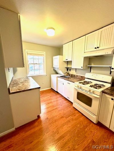 Kitchen featuring stacked washer and dryer, white gas stove, sink, white cabinetry | Image 3