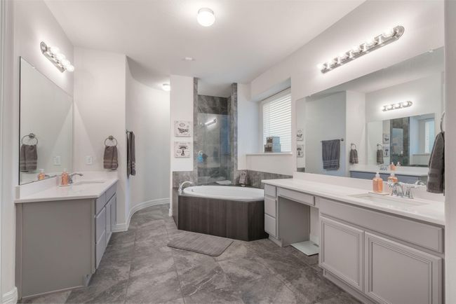 Master bathroom with dual vanities, ample counter space, a luxurious soaking tub, and modern tile flooring. The soft lighting and neutral color palette create a relaxing atmosphere. | Image 23