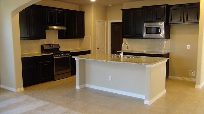 Kitchen with appliances with stainless steel finishes, a sink, under cabinet range hood, tasteful backsplash, and light stone counters | Image 5