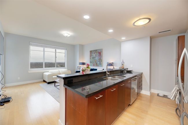 Kitchen with light wood finished floors, dishwasher, open floor plan, a peninsula, and dark stone countertops | Image 9