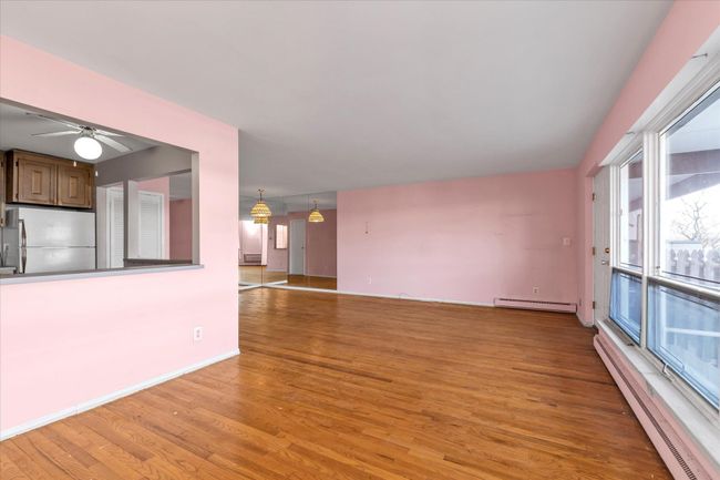 Unfurnished living room with light wood-type flooring, a baseboard radiator, ceiling fan, and baseboards | Image 9