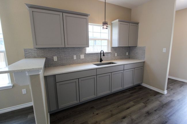 Kitchen with gray cabinetry, tasteful backsplash, dark wood finished floors, and light countertops | Image 7