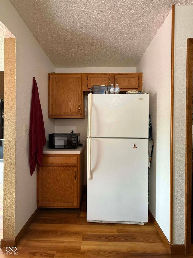 kitchen featuring freestanding refrigerator, black microwave, a textured ceiling, wood finished floors, and brown cabinetry | Image 24
