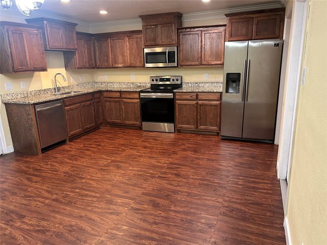 Kitchen featuring appliances with stainless steel finishes, crown molding, dark wood finished floors, recessed lighting, and light stone counters | Image 6