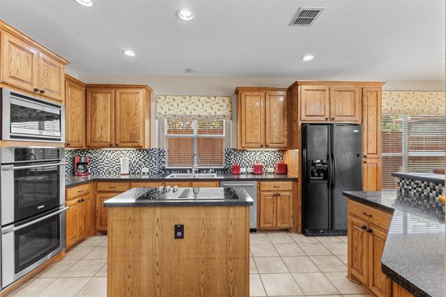 Kitchen with black appliances, a sink, a kitchen island, light tile patterned floors, and decorative backsplash | Image 8