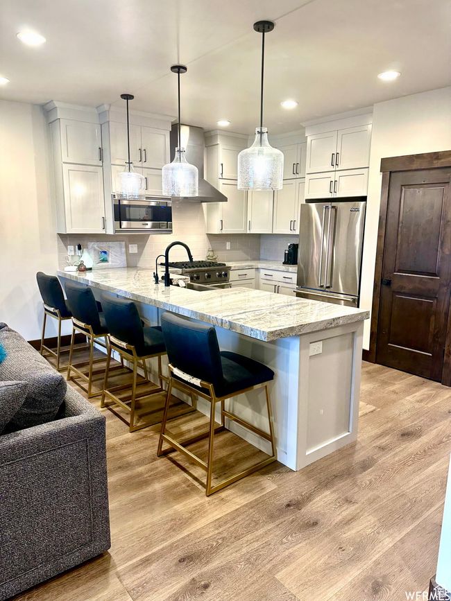 Kitchen featuring a breakfast bar area, premium appliances, pendant lighting, light hardwood / wood-style floors, and light great cabinets | Image 4