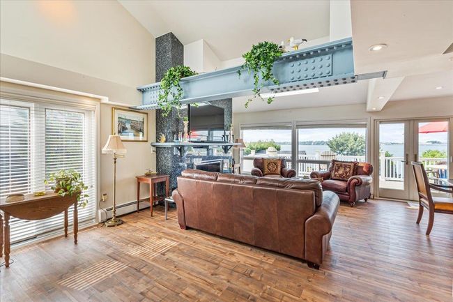 Living area with high vaulted ceiling, wood finished floors, a fireplace, a baseboard heating unit, and french doors | Image 6