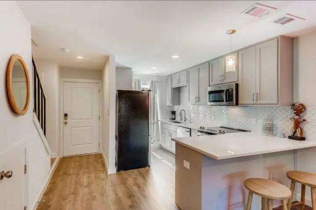 Kitchen with freestanding refrigerator, stainless steel microwave, gray cabinets, a breakfast bar area, and decorative backsplash | Image 11