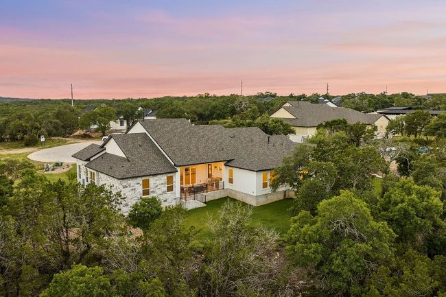 Back of property at dusk featuring stone siding, roof with shingles, stucco siding, and view of wooded area | Image 38