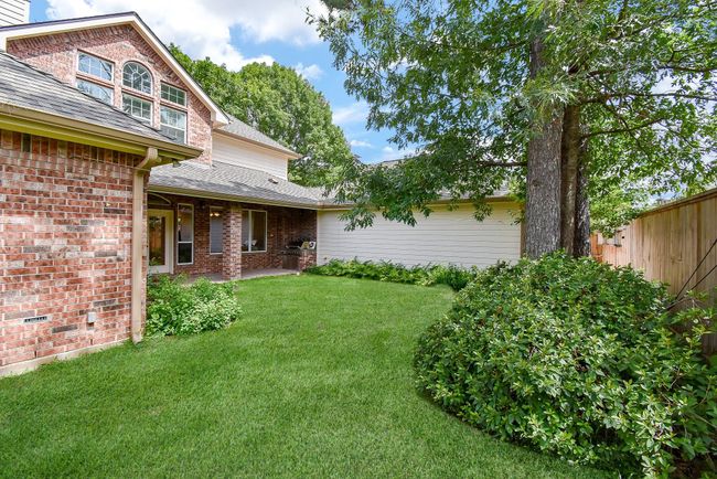 This photo showcases a charming brick home with a well-maintained backyard. The green lawn is bordered by lush bushes and shaded by a large tree. A wooden fence provides privacy, and the architecture features multiple windows for natural light. | Image 48