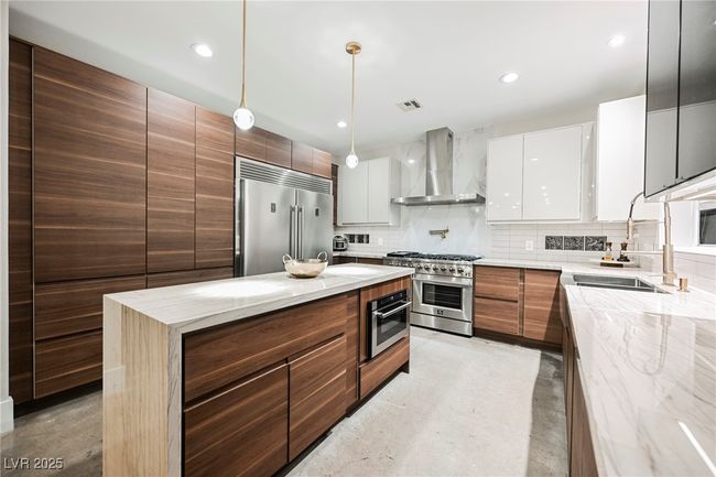 Kitchen featuring wall chimney range hood, visible vents, modern cabinets, premium appliances, and a sink | Image 13