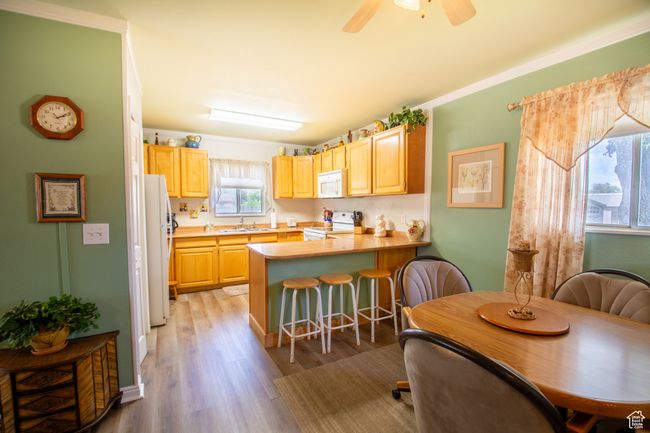Kitchen with white appliances, light brown cabinets, a peninsula, a breakfast bar, and light wood-style floors | Image 10