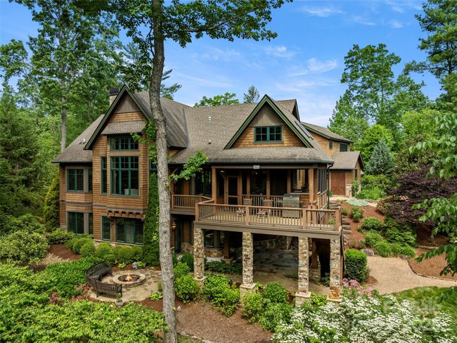 View of exterior of house which shows the soaring living room windows, partially covered upper deck, covered terrace level patio and stone fire pit. | Image 40