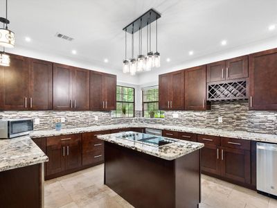 Modern kitchen with dark wood cabinets, granite countertops, stainless steel appliances, and a mosaic tile backsplash. Bright and spacious with pendant lighting. | Image 2