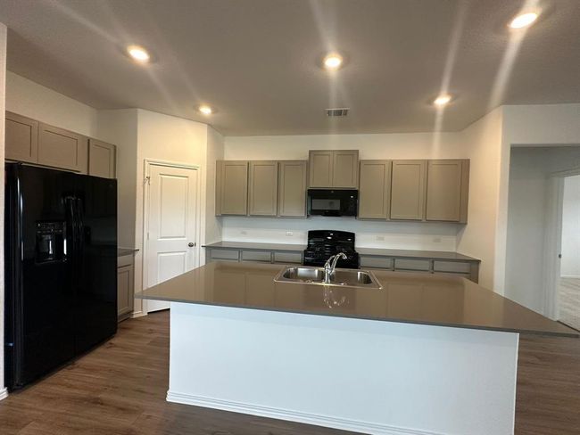 Kitchen with black appliances, a sink, gray cabinetry, dark wood-type flooring, and a center island with sink | Image 15