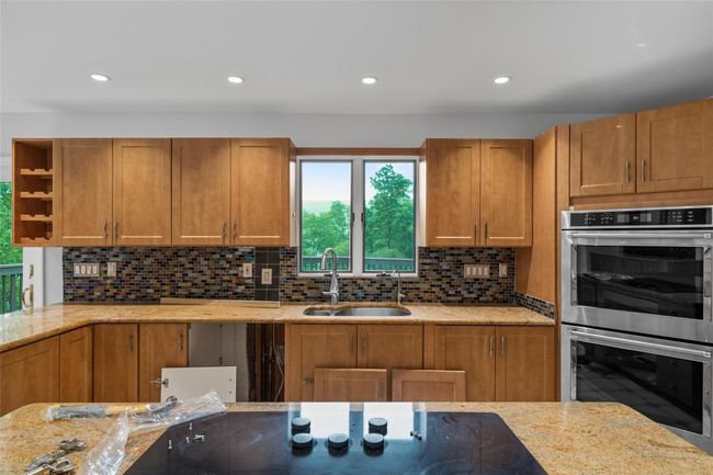 Kitchen with stainless steel double oven, backsplash, light stone counters, recessed lighting, and open shelves | Image 9