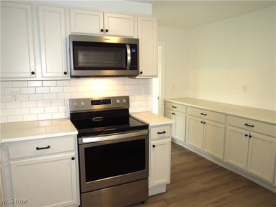 Kitchen featuring stainless steel appliances, dark hardwood / wood-style floors, white cabinets, and tasteful backsplash | Image 3