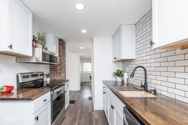 kitchen featuring butcher block counters, tasteful backsplash, stainless steel appliances, and a sink | Image 9