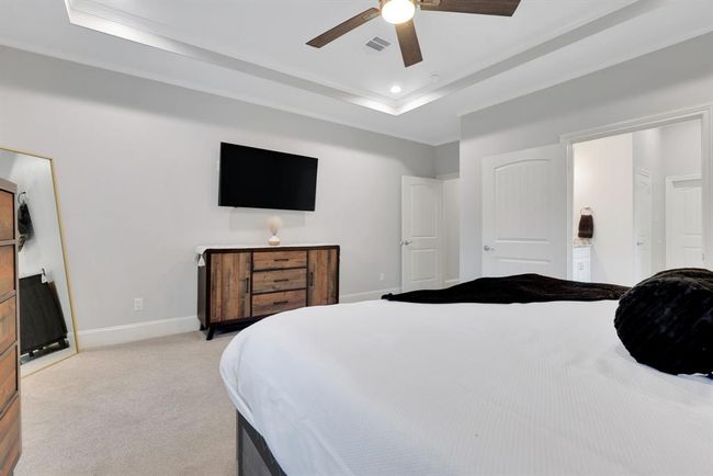 This serene primary suite offers tray ceilings, a luxurious en suite bath, and large windows that showcase the tranquil backyard setting. | Image 23
