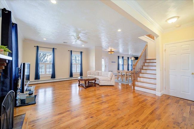 Living area featuring ceiling fan, light wood-style floors, baseboard heating, crown molding, and stairs | Image 10