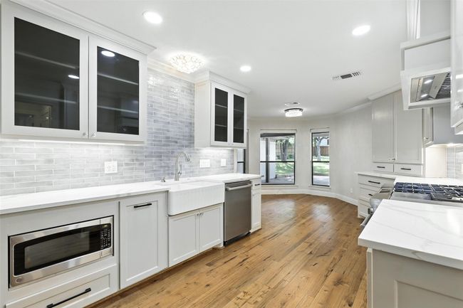 Kitchen featuring appliances with stainless steel finishes, decorative backsplash, white cabinets, ornamental molding, and light wood-style floors | Image 14