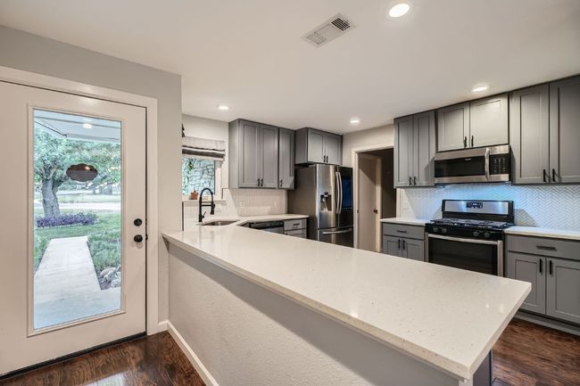 Kitchen with stainless steel appliances, gray cabinetry, decorative backsplash, dark wood finished floors, and recessed lighting | Image 6