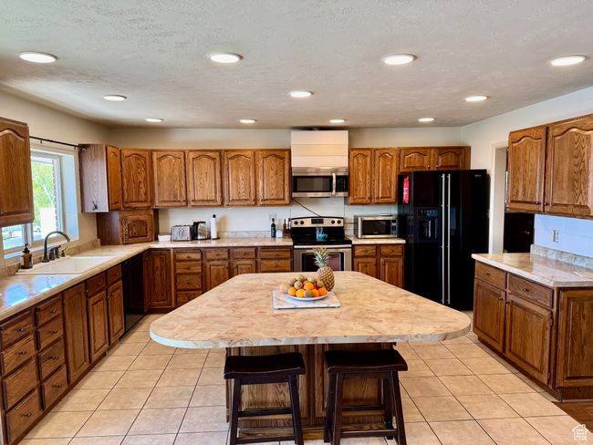 Kitchen with light tile patterned floors, brown cabinets, a sink, light countertops, and black appliances | Image 5