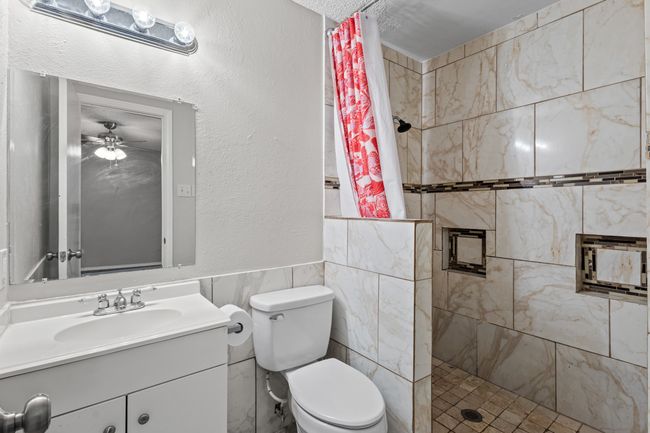 Bathroom with a tile shower, tile walls, vanity, toilet, and ceiling fan | Image 18