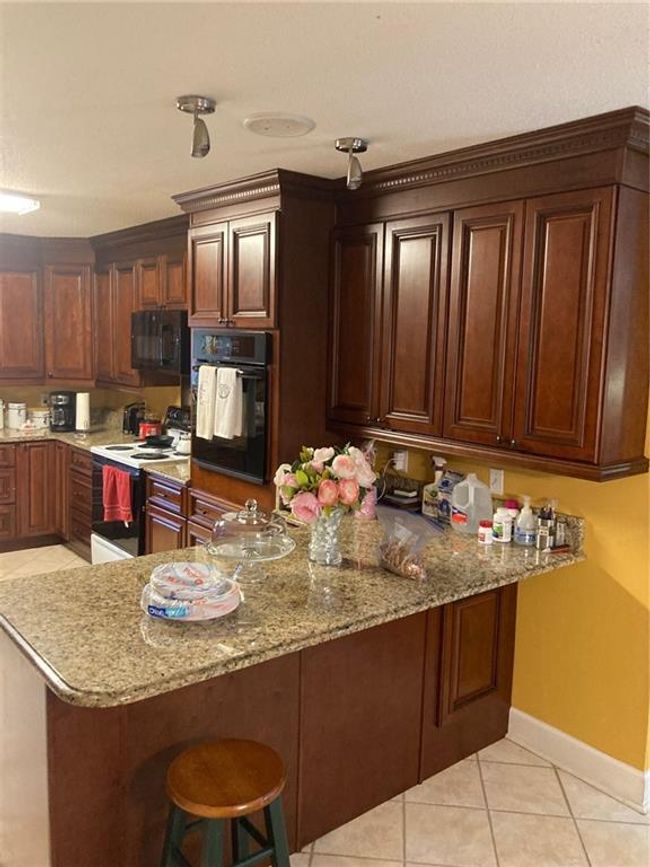 Kitchen featuring wall oven, kitchen peninsula, light stone counters, and stove | Image 9