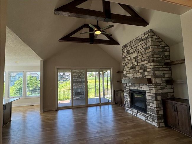 Unfurnished living room with plenty of natural light, wood finished floors, a fireplace, beam ceiling, and a ceiling fan | Image 7