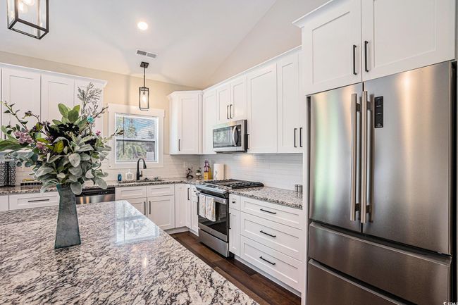 Kitchen featuring stainless steel appliances, lofted ceiling, backsplash, white cabinets, and dark wood-style flooring | Image 9