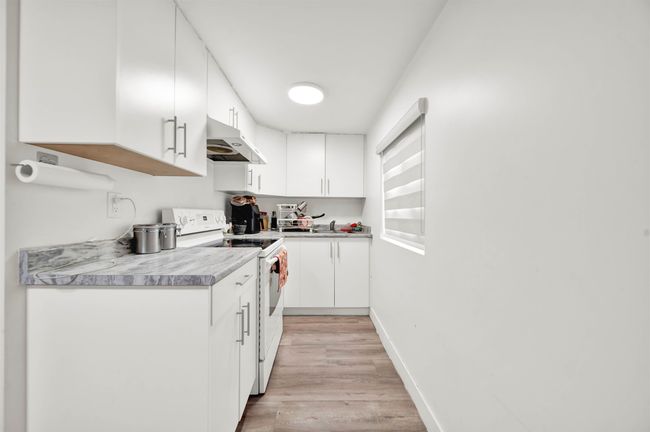 Kitchen featuring electric stove, under cabinet range hood, light wood-style floors, white cabinetry, and baseboards | Image 13